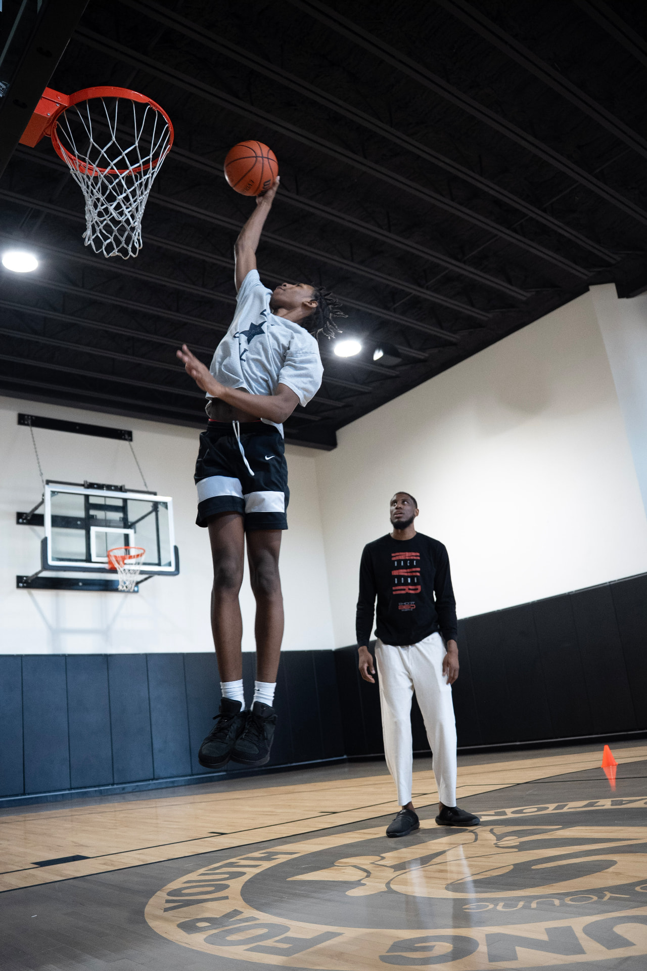 Young player finishing at the rim while a coach observes